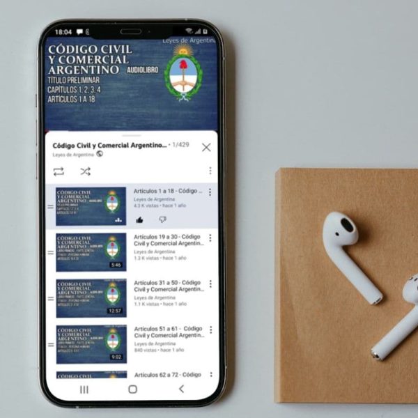 Celular en el que se reproduce el audiolibro del Código Civil y Comercial Argentino, junto a unos auriculares inalámbricos.