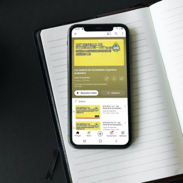 Un celular apoyado sobre un cuaderno reproduce el audiolibro de la Ley General de Sociedades.